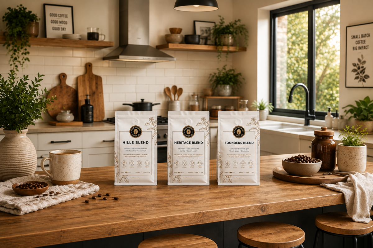 Three bags of coffee beans labeled Hills Blend, Heritage Blend, and Foundry Blend are displayed on a wooden kitchen island, with a warm, modern kitchen in the background.