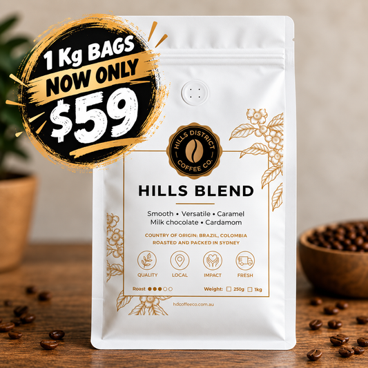 A 1 kg bag of Hills District Coffee Co. Hills Blend coffee sits on a wooden surface with scattered coffee beans.