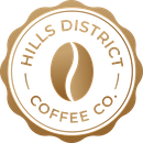 A circular gold seal logo for Hills District Coffee Co., featuring a stylized coffee bean in the center and the text 'HILLS DISTRICT COFFEE CO.