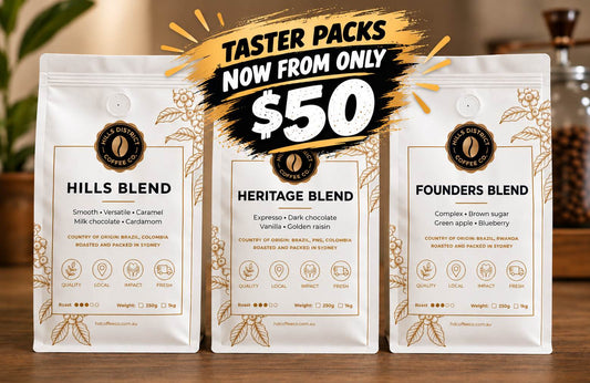 Three bags of Hills Coffee Company blends (Hills Blend, Heritage Blend, Founders Blend) displayed on a wooden table with a promotional graphic overlay at the top.